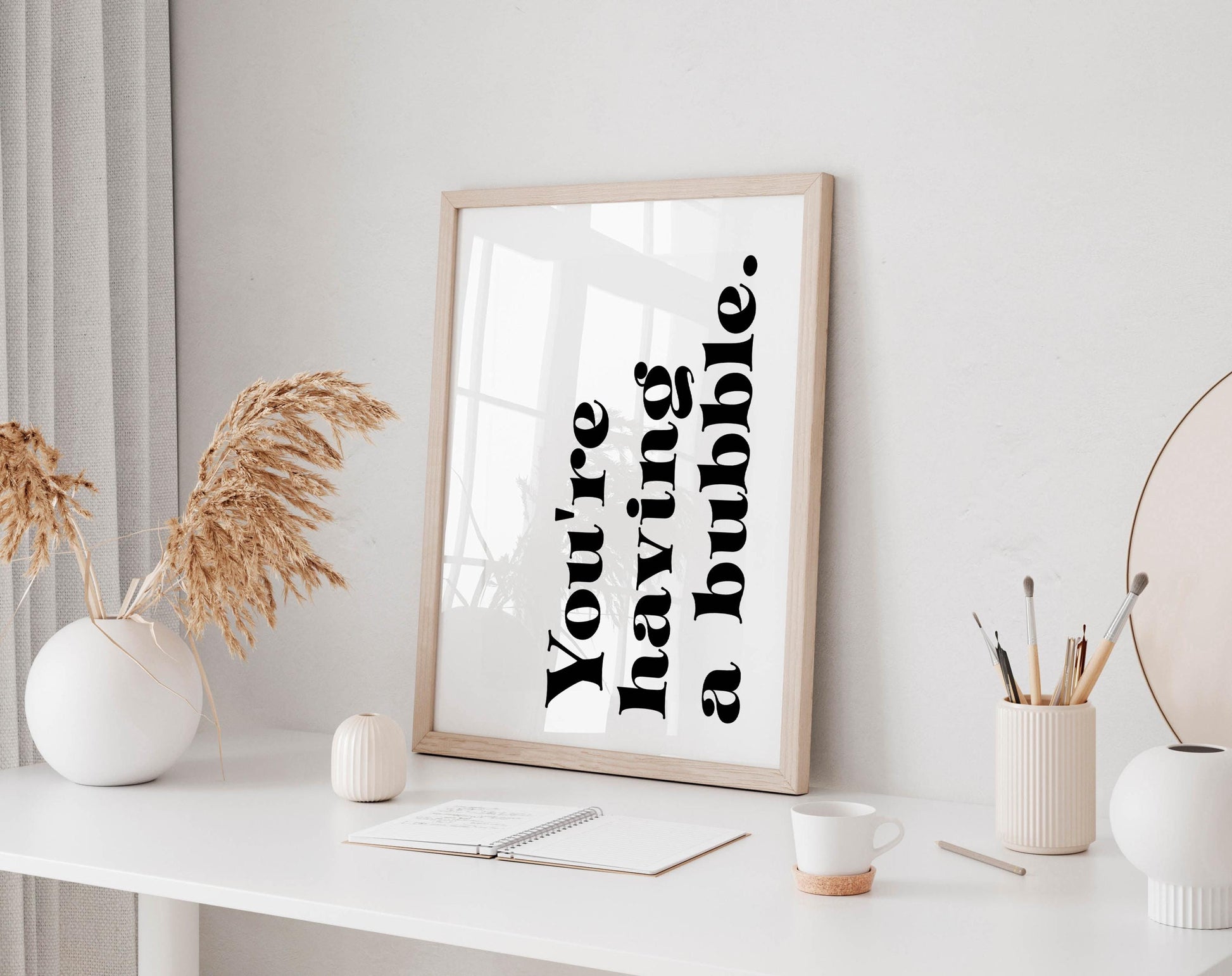 a white desk with a framed quote, a small white vase with dried flowers, a white mug, a small white candle, and a small white candle holder.