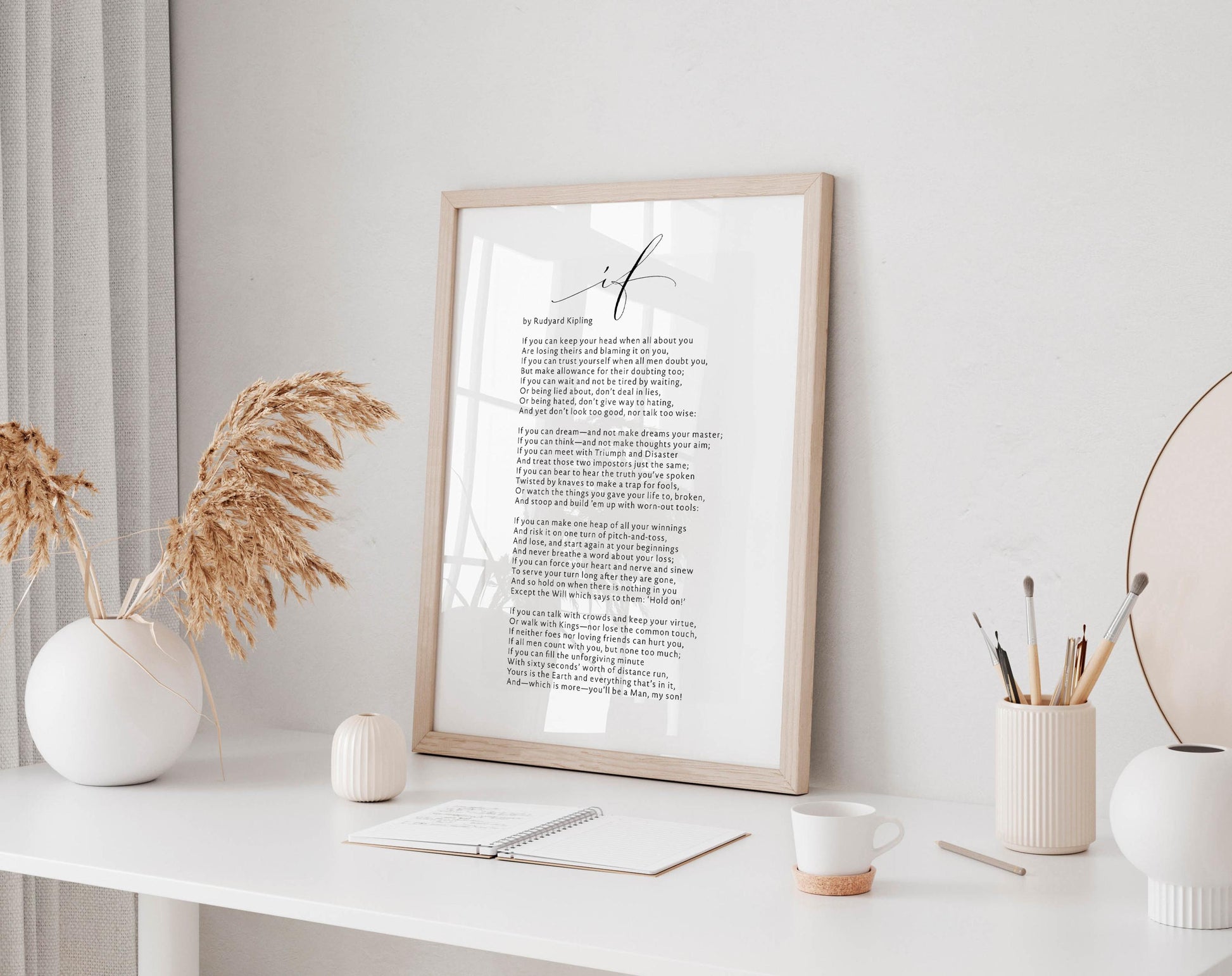 a framed poem titled &quot;I am&quot; displayed on a white desk, accompanied by a notebook, a cup, and a vase with dried flowers.
