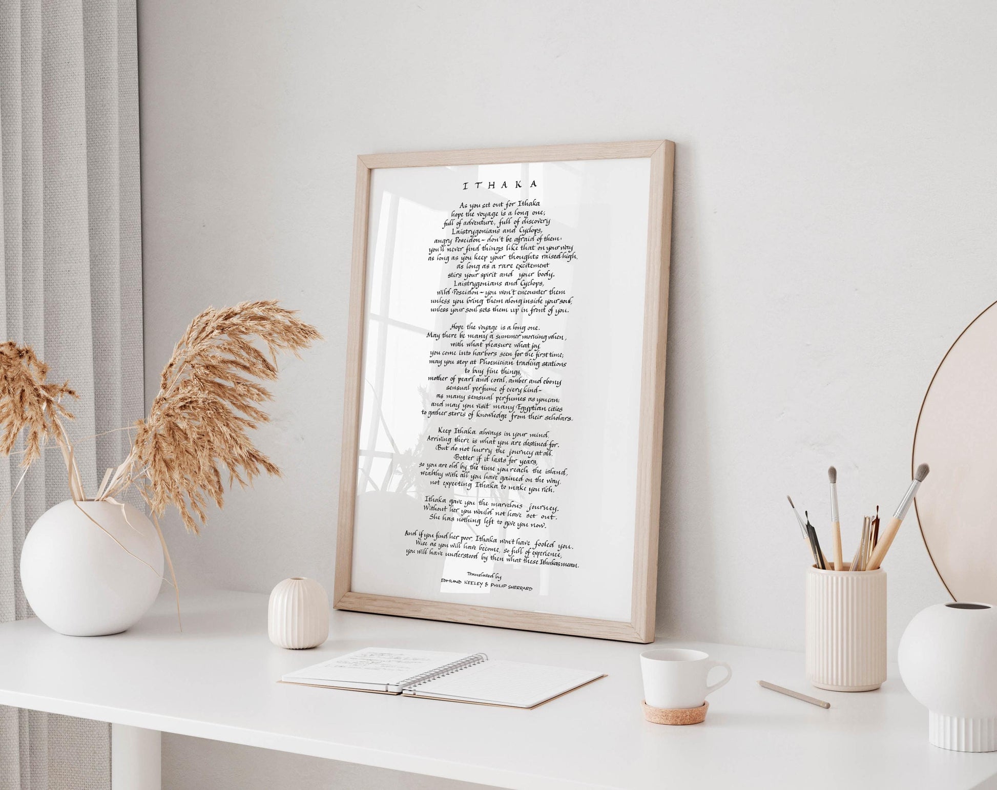 a framed poem titled &quot;Ita&#39;ka&quot; displayed on a white desk, surrounded by various objects such as a notebook, a cup, and a vase with dried flowers.