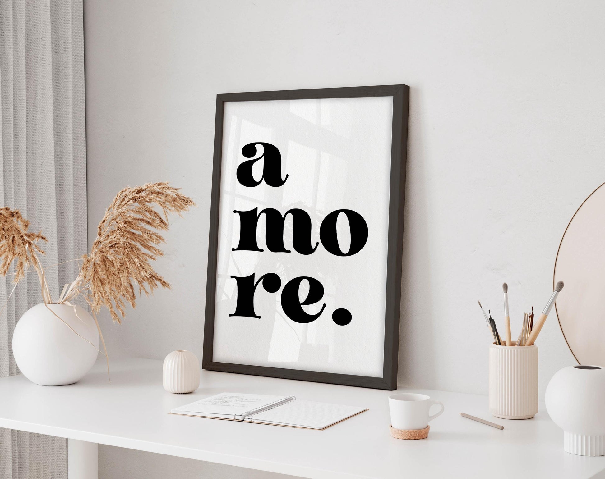 a white desk with a framed poster displaying the text &quot;a more.&quot; The desk also has various items such as a cup, a notebook, and a vase with dried flowers.