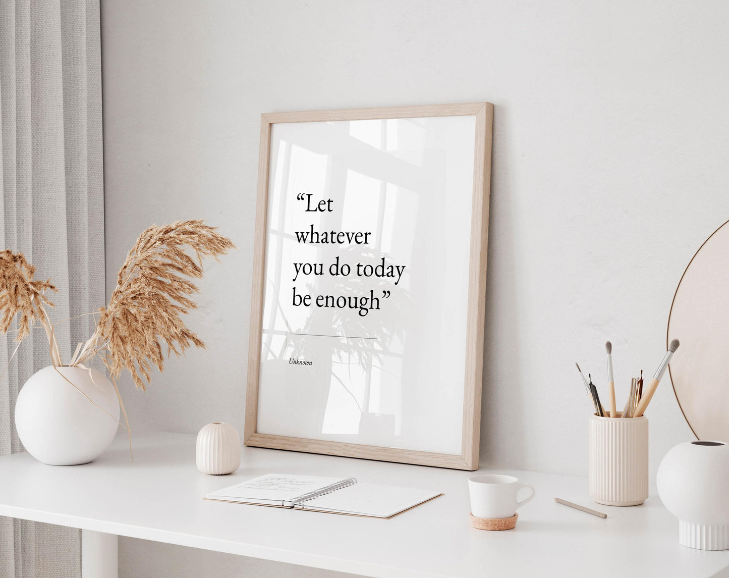 a white desk with a framed quote, a notebook, a cup, and a vase with dried flowers.