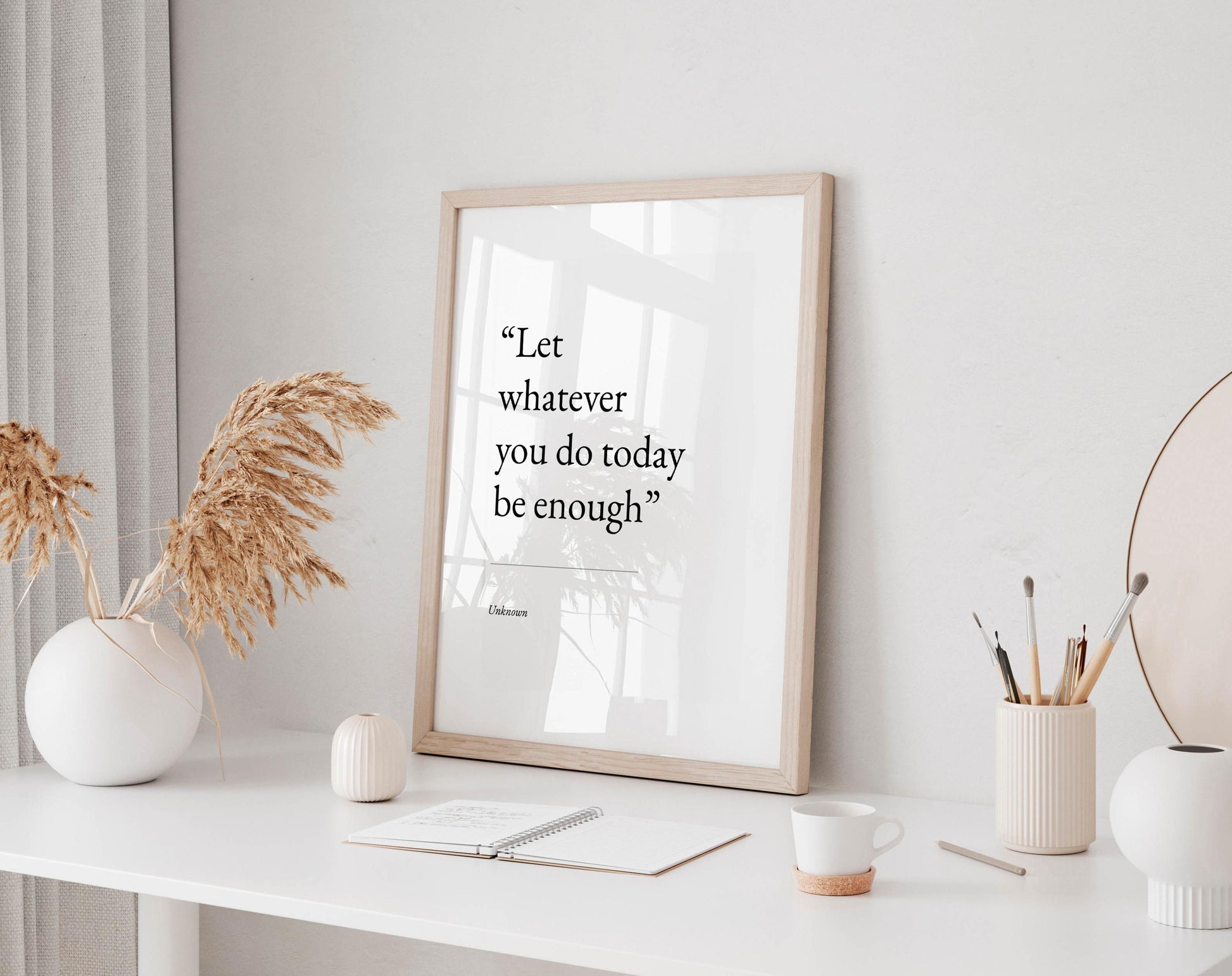 a white desk with a framed quote, a notebook, a cup, and a vase with dried flowers.