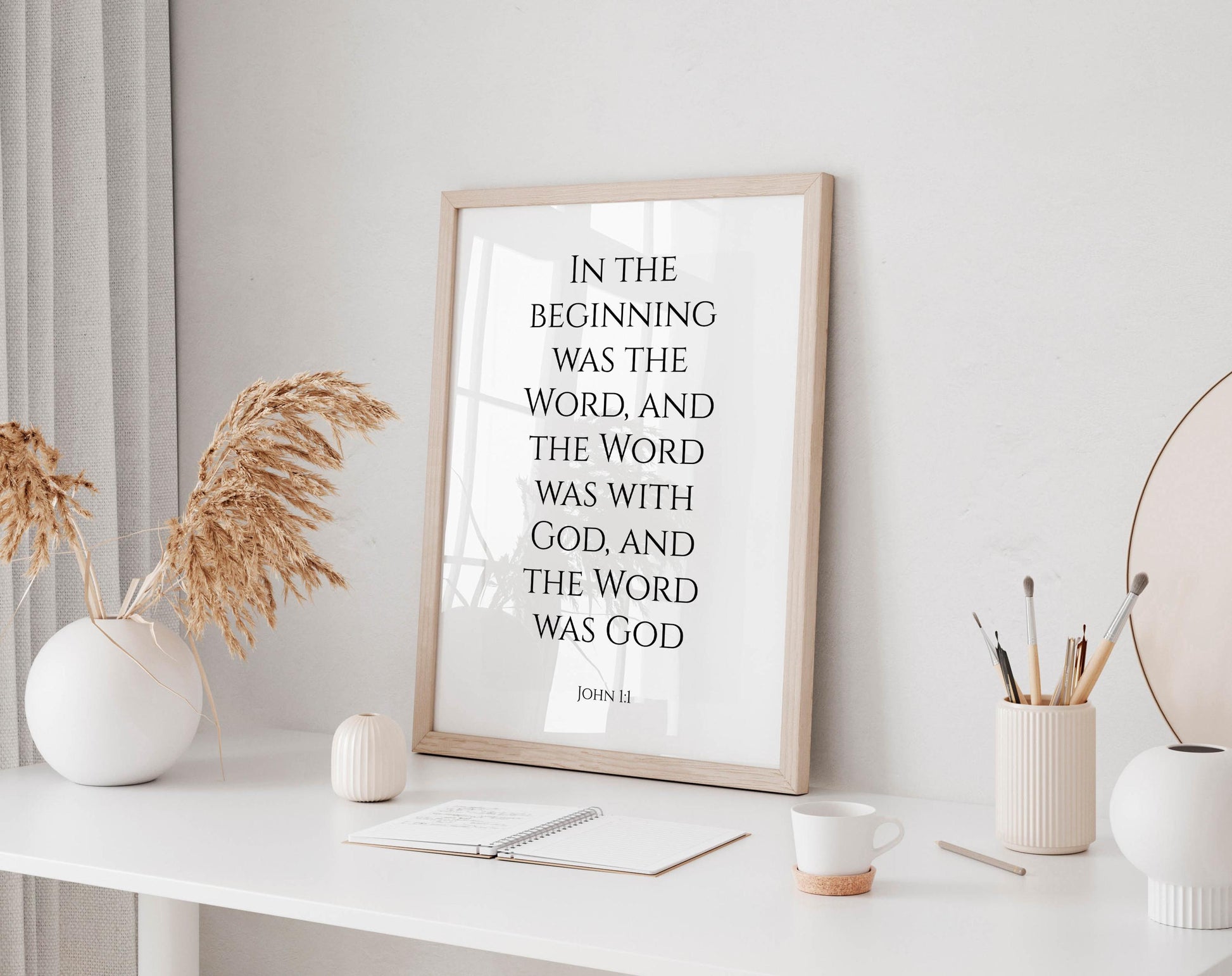 a framed quote on a white desk, surrounded by various objects such as a notebook, a cup, and a vase with dried flowers.