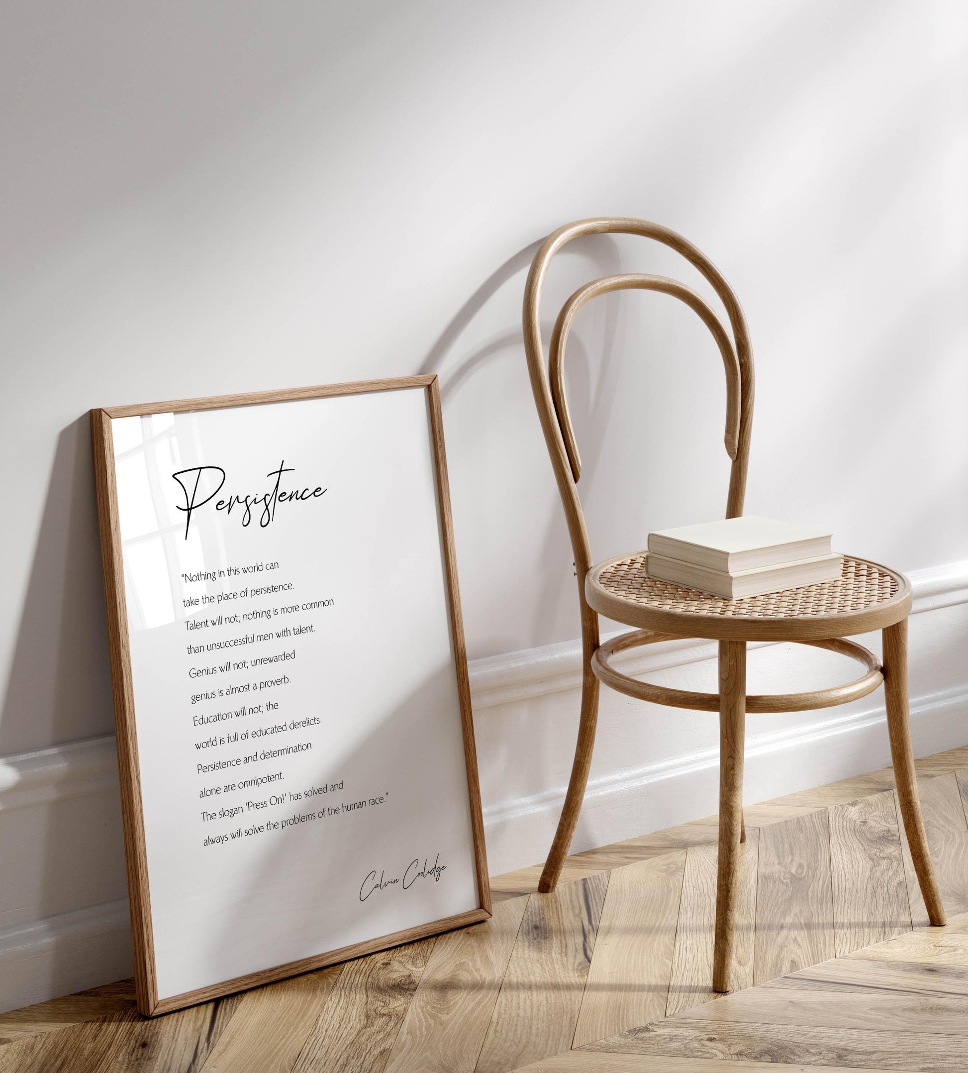 a framed quote titled &quot;PERSISTENCE&quot; leaning against a wooden chair, with a stack of books on the chair&#39;s seat.