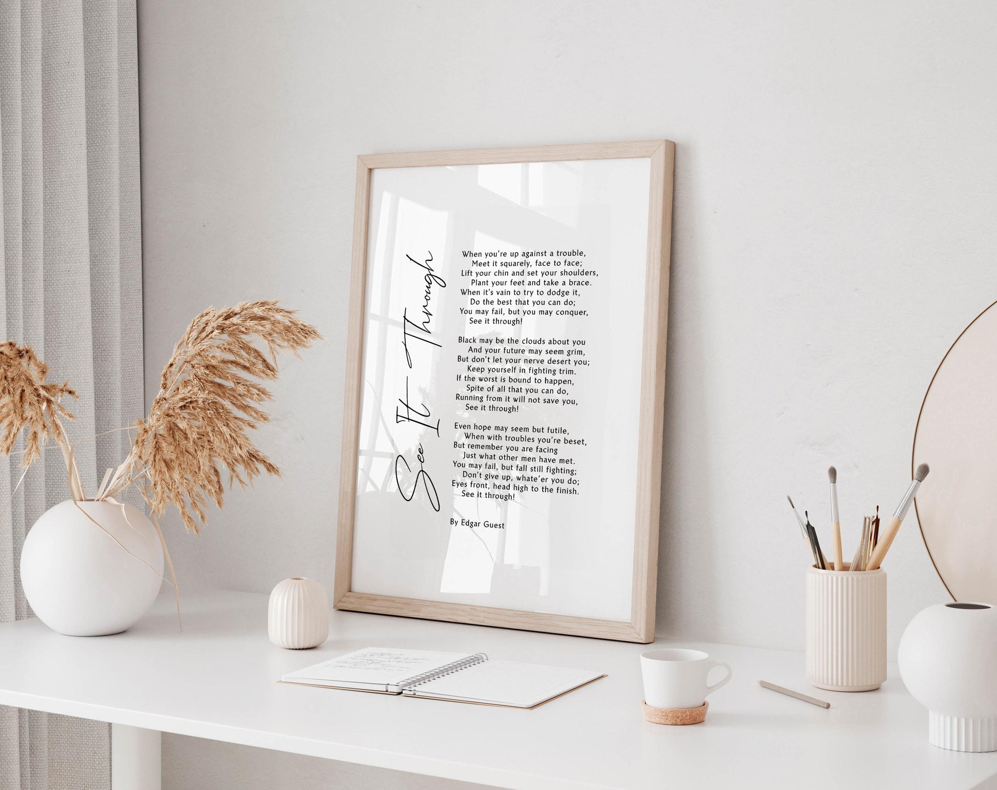 a framed poem titled &quot;See It Through&quot; displayed on a white desk, accompanied by a notebook, a cup, and a vase with dried flowers.