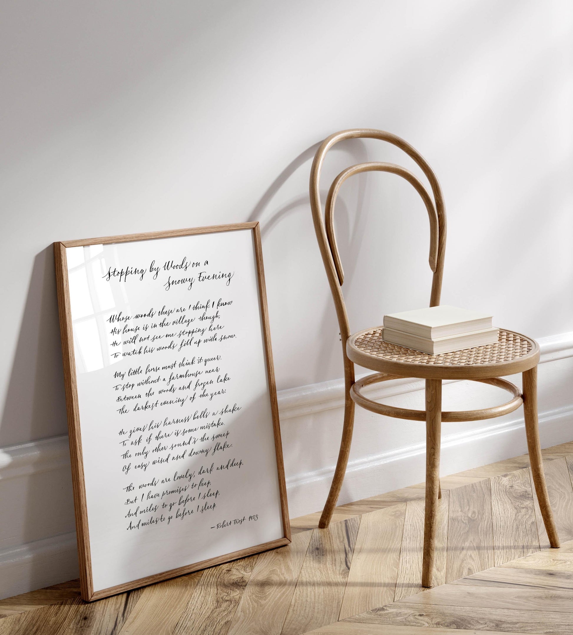 A framed poem titled &quot;Stopping by Woods on a Snowy Evening&quot; is leaning against a wooden chair on a wooden floor.