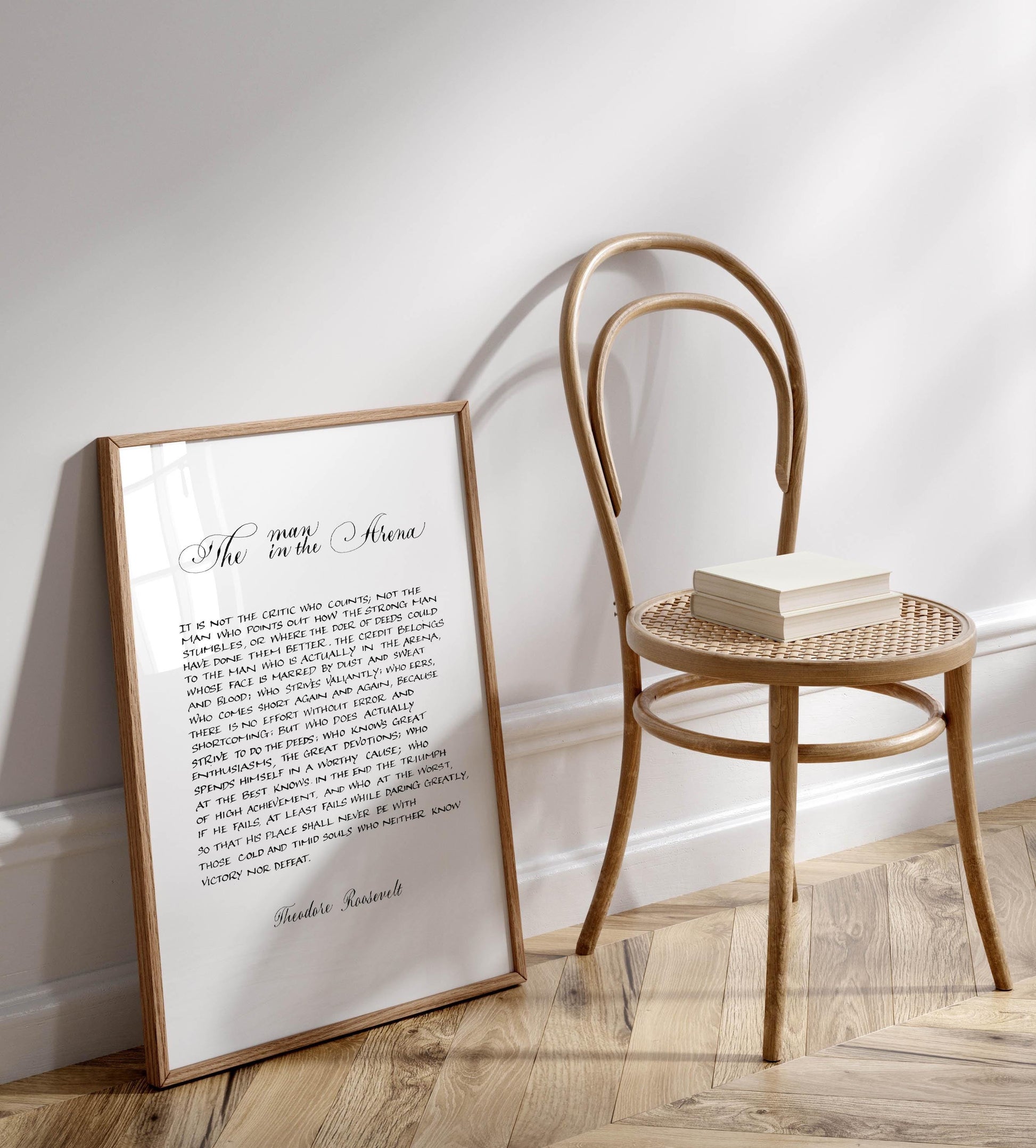 a framed quote by Theodore Roosevelt, &quot;The man in the Arena&quot; - a quote about courage and the importance of facing one&#39;s fears. The quote is displayed on a white wall, with a wooden chair positioned next to it.