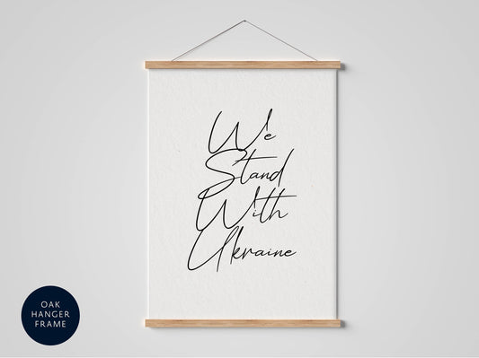 a white poster with black cursive text that reads &quot;We Stand with Ukraine&quot; hanging on a wall.