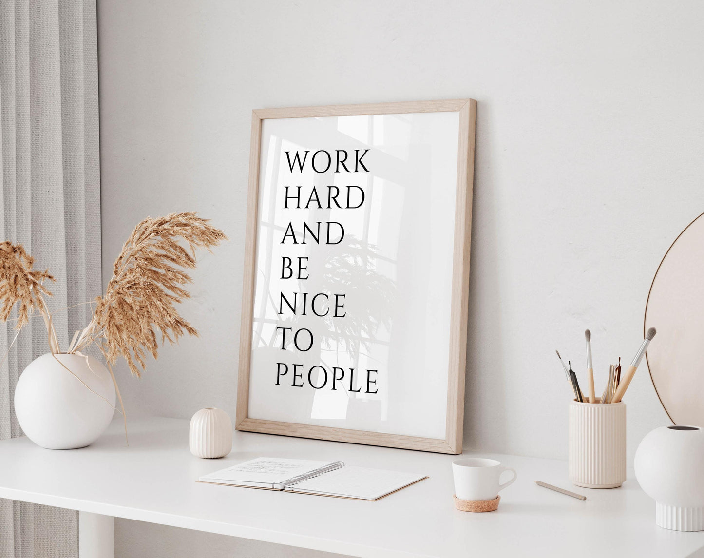 a white desk with a framed motivational quote, a notebook, a cup, and a vase with dried flowers.