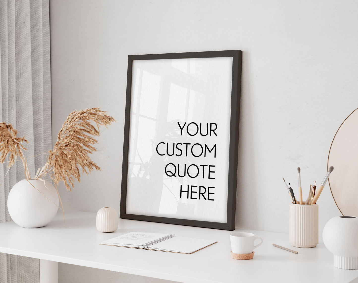 a white desk with a framed quote that reads &quot;YOUR CUSTOM QUOTE HERE&quot; in bold black text. The desk also has a few decorative items, including a vase with dried flowers, a small white candle, and a white mug.
