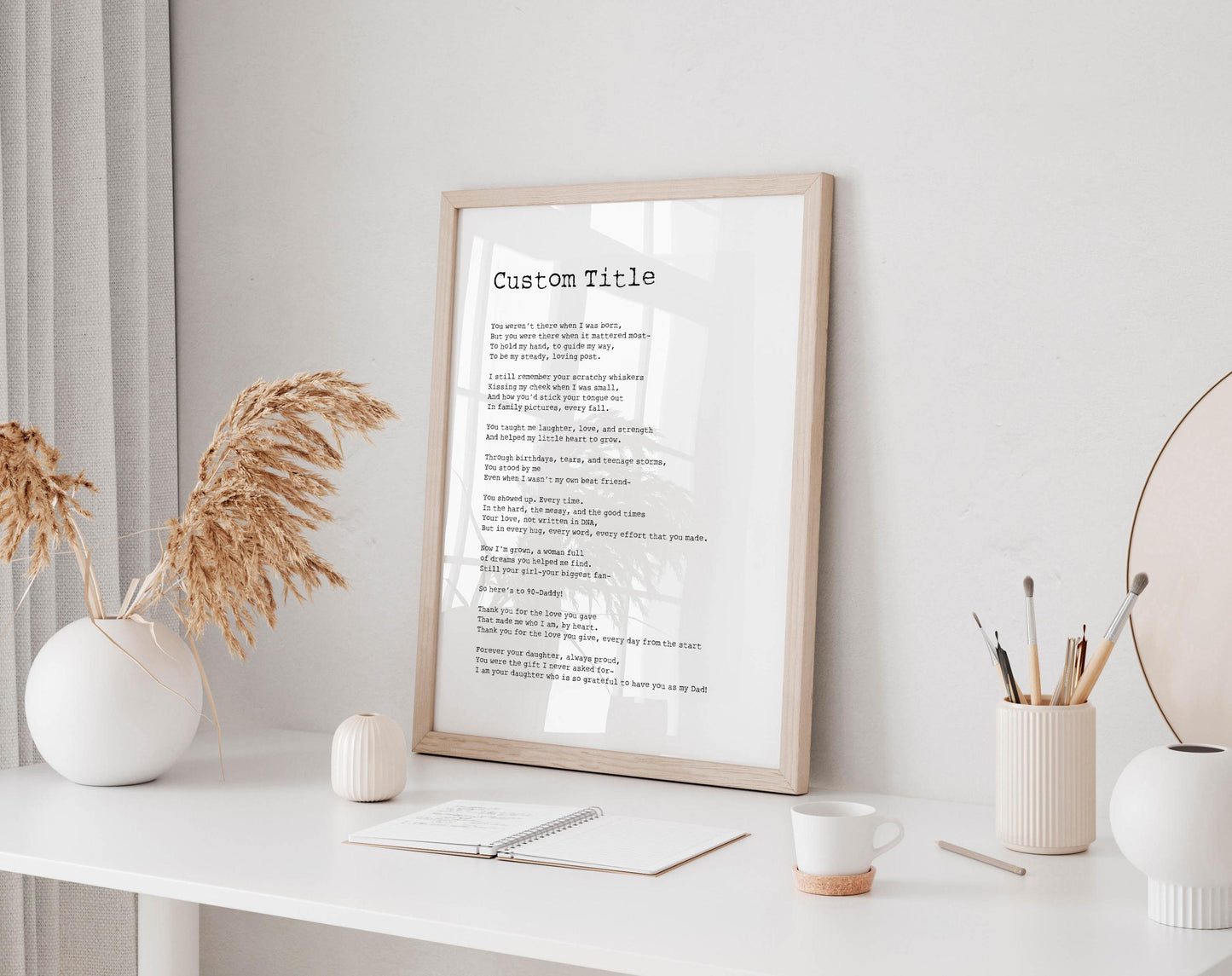 a framed poem titled "Custom Title" displayed on a white desk, accompanied by a notebook, a cup, and a vase with dried flowers.