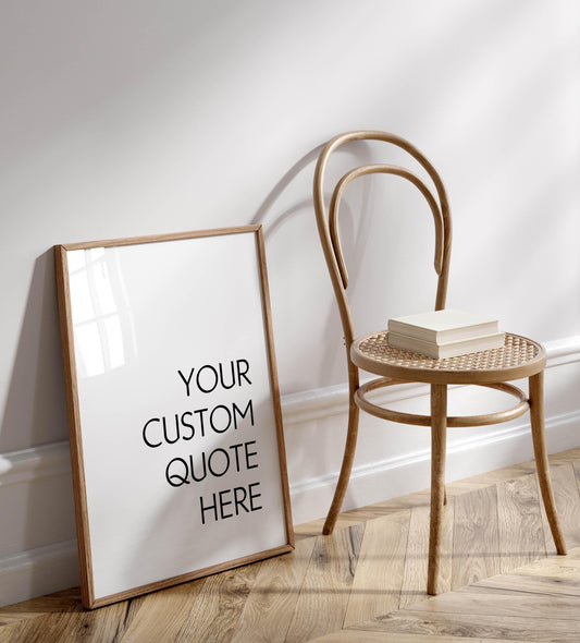 a white wall with a wooden chair and a white picture frame with the text "YOUR CUSTOM QUOTE HERE" on it.