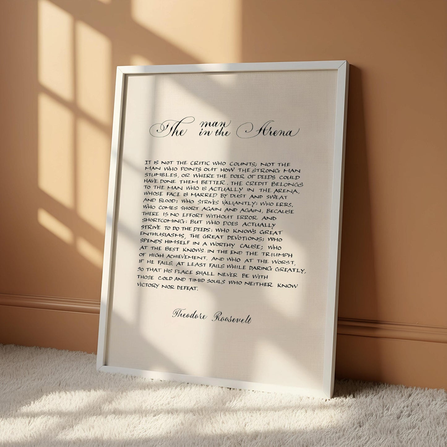 a framed text that reads "The man in the arena" and is written in cursive. The text is framed by a wooden border and is set against a white background.