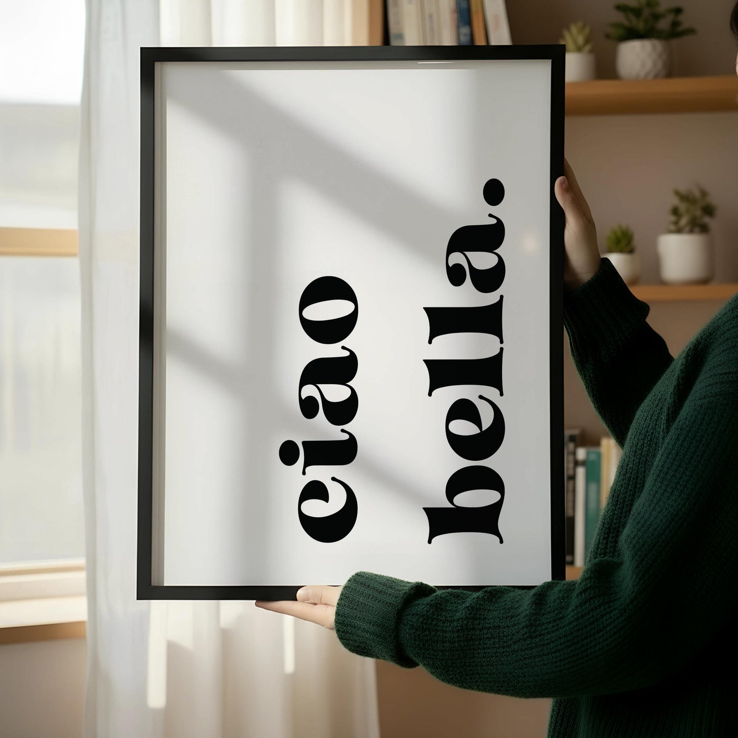 a wooden chair with a book on it, placed next to a framed poster with the text "eiao bella" on it, which is leaning against a white wall.