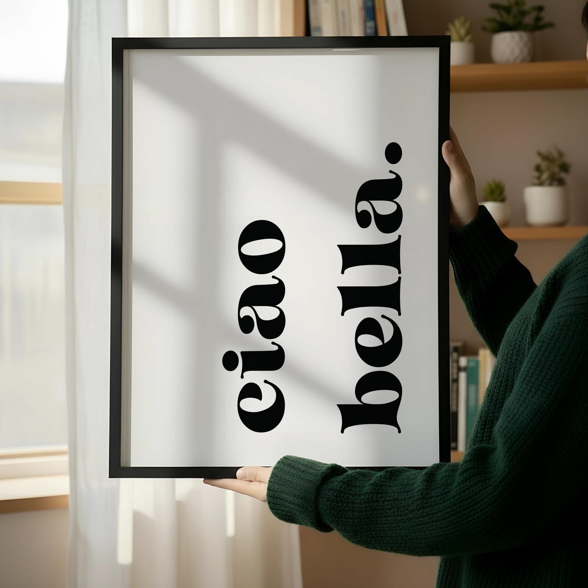a wooden chair with a book on it, placed next to a framed poster with the text "eiao bella" on it, which is leaning against a white wall.