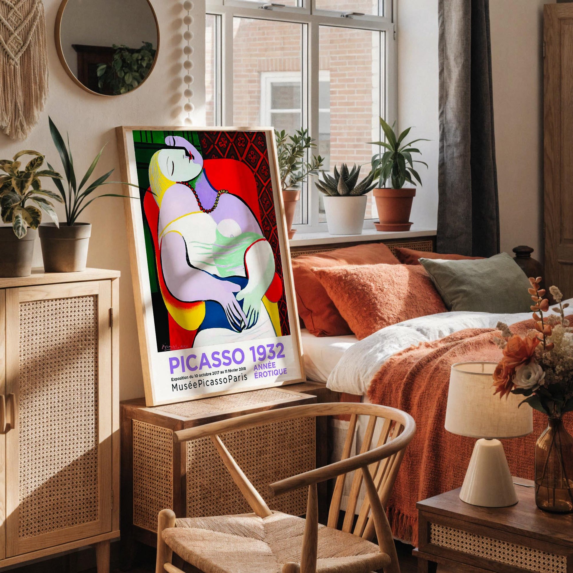 a framed poster of Picasso's cubist artwork, which is displayed on a white desk. The poster is surrounded by various objects, including a white vase, a small white candle, a white mug, and a white notebook.