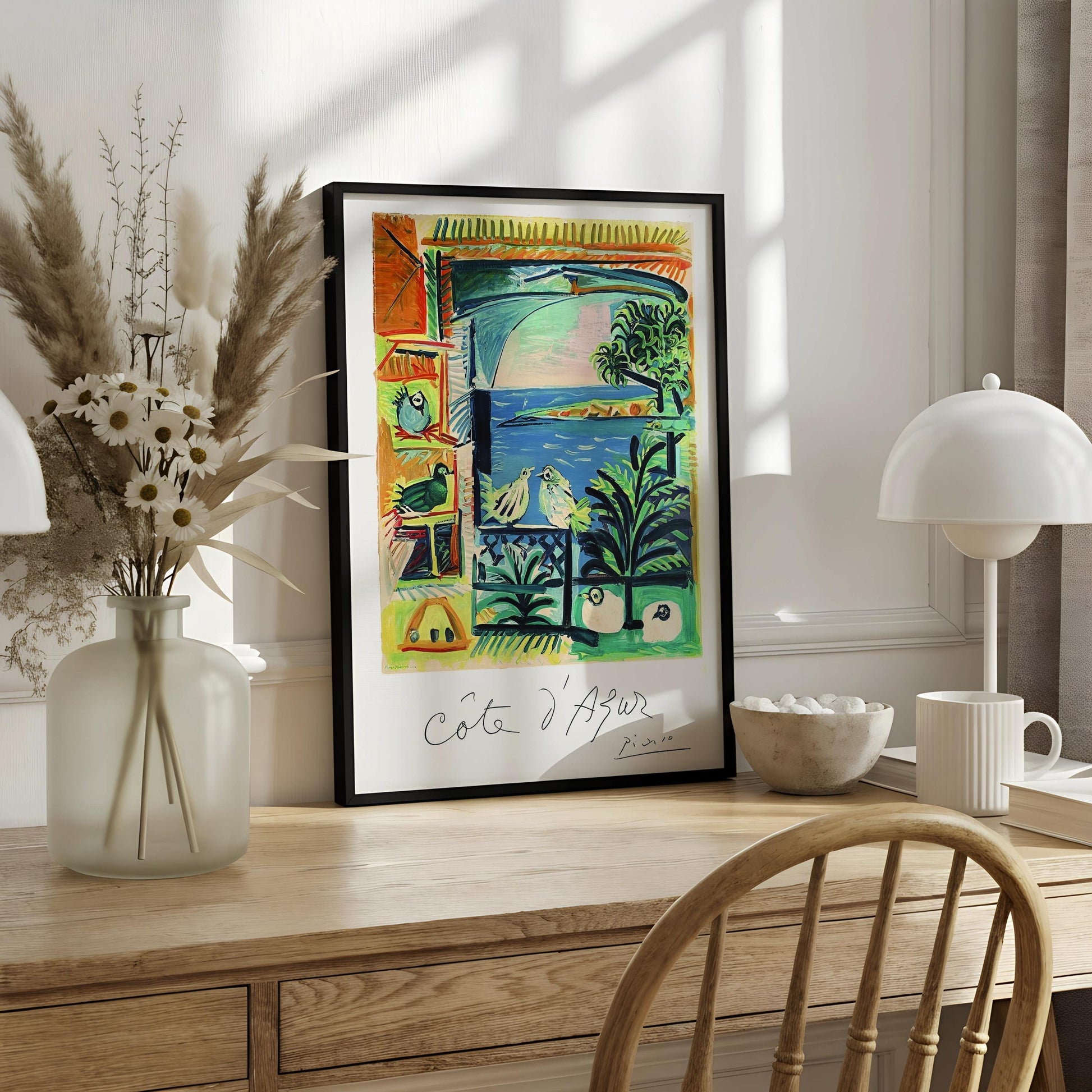 The image is a framed painting hanging on a wall, depicting a colorful and vibrant scene with various elements such as birds, plants, and a body of water.