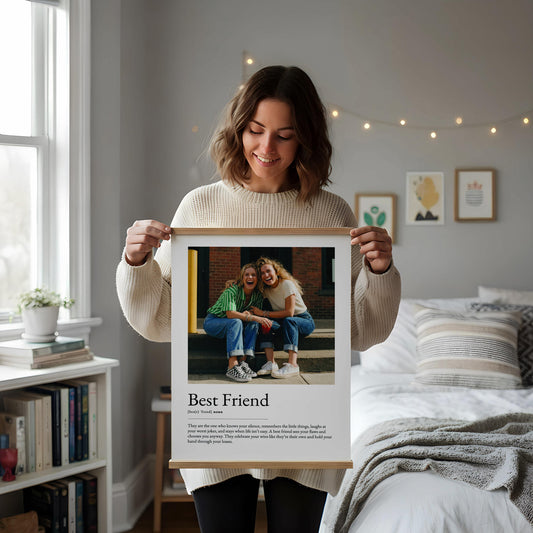 May include: A framed print with the text "Best Friend" and a definition. The print features a photo of two smiling people. The frame is made of light-coloured wood. The background includes a window, a bookshelf, and a bed.