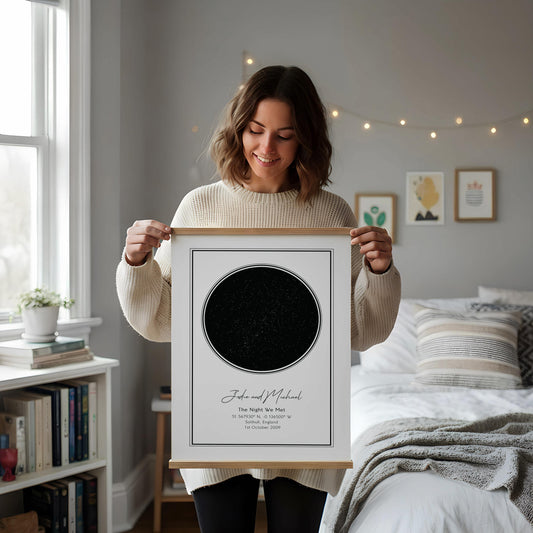 a framed picture of a starry night sky on a white desk, accompanied by a notebook, a cup, and a vase with dried flowers.