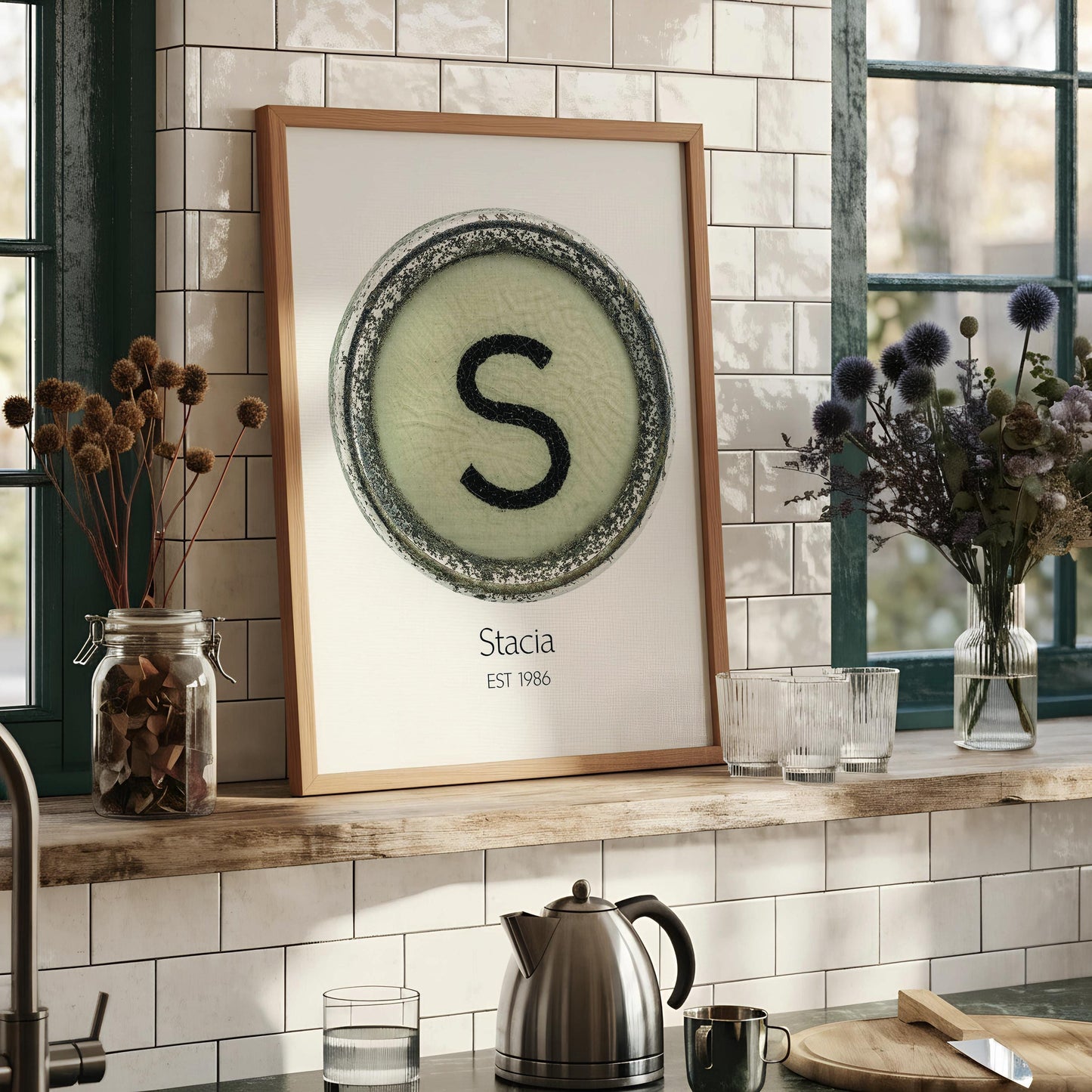 a framed print with a circular design containing a large letter 'S' in the center, surrounded by a decorative border. The print is titled "Stacia" and is framed in an oak-colored frame.