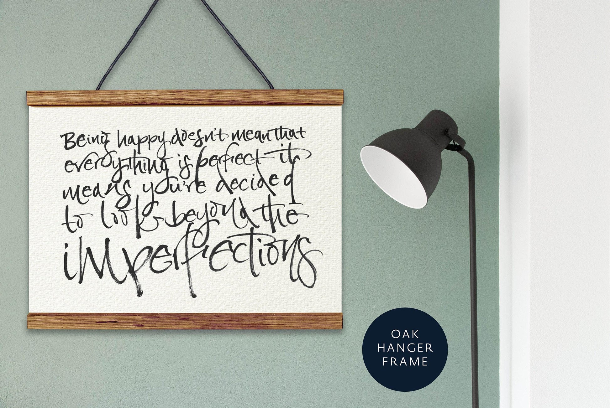 a wooden frame hanging on a wall, with a black lamp standing next to it. The wall has a greenish-blue color, and there is a quote written on the frame.