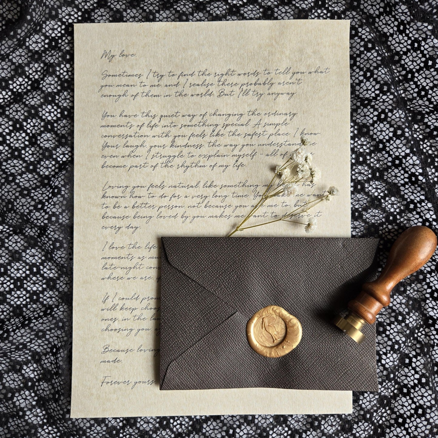 a handwritten letter, a wax seal, and a wooden stamp on a black and white patterned fabric.