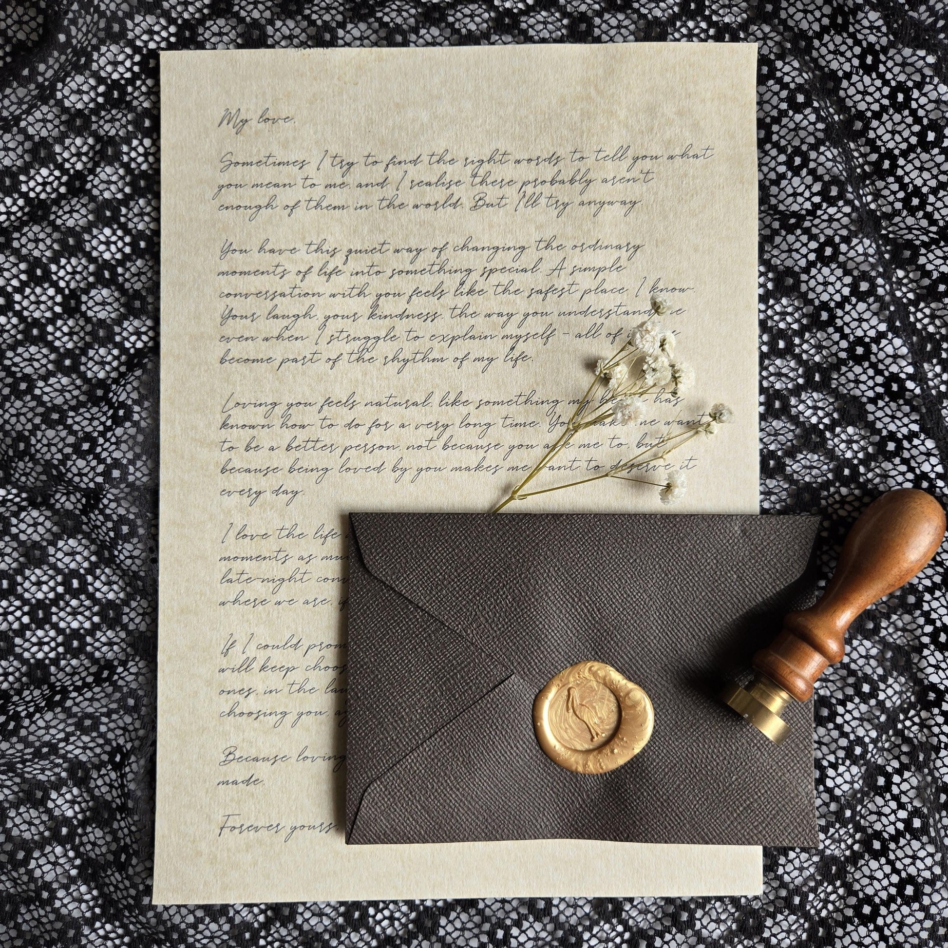 a handwritten letter, a wax seal, and a wooden stamp on a black and white patterned fabric.