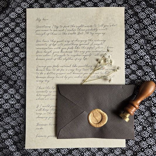 a handwritten letter, a wax seal, and a wooden stamp on a black and white patterned fabric.