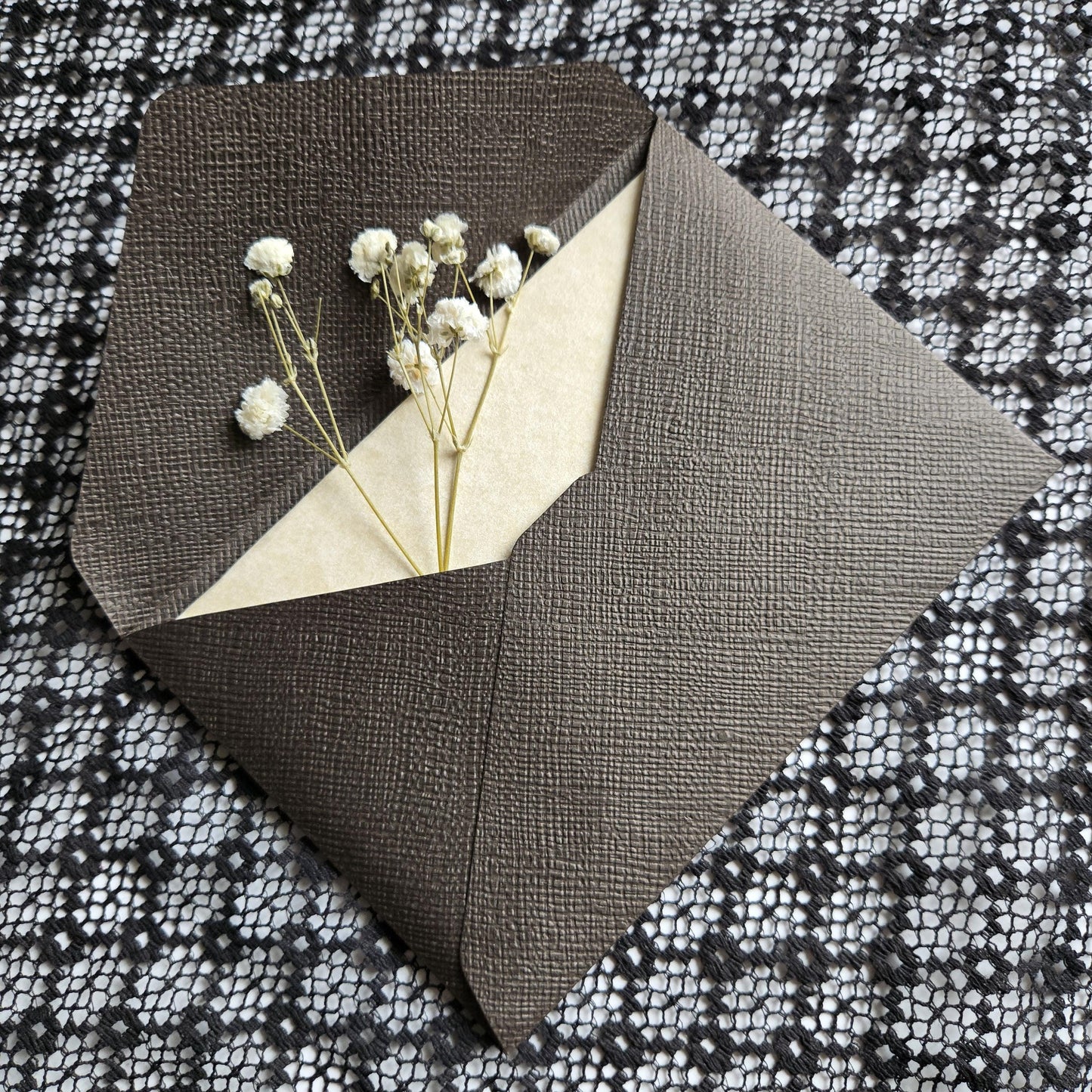a small bouquet of white flowers placed inside an envelope, which is resting on a black and white patterned fabric.