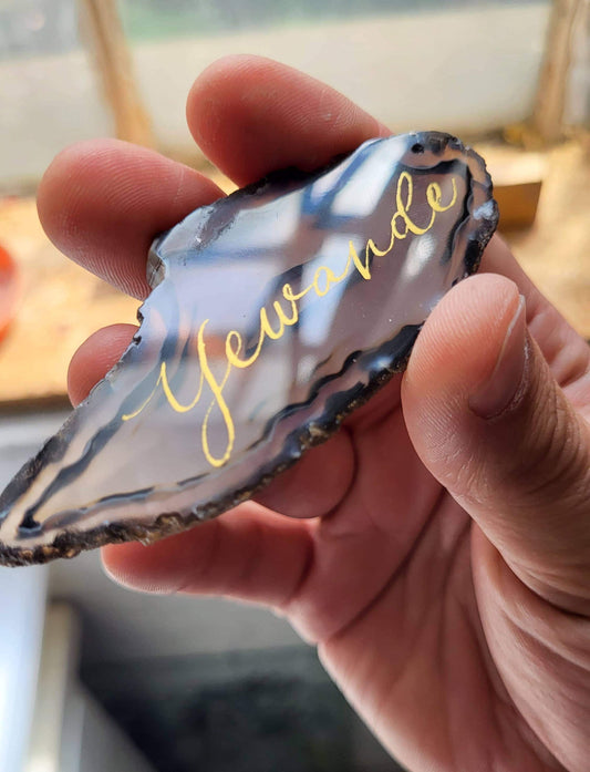 A hand holding a piece of rock with the word "Yewande" written on it.
