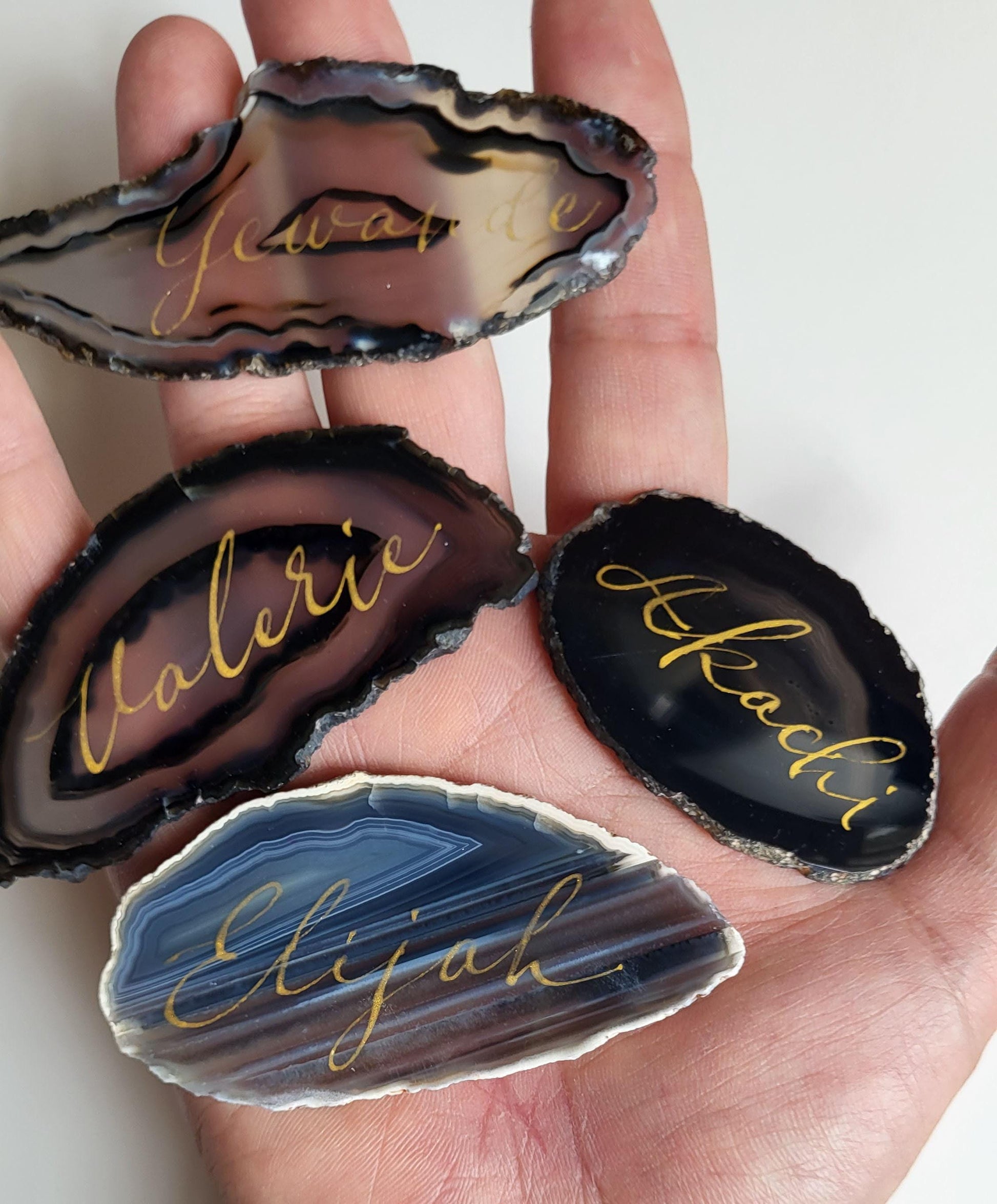 A hand holding four unique nameplate-shaped stones with personalized names engraved on them.