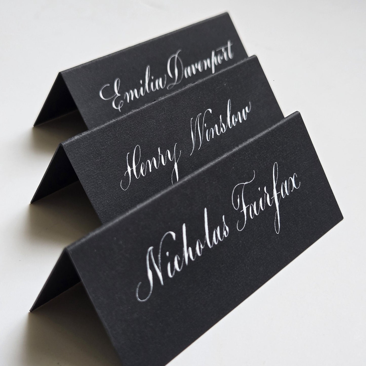 three black name cards with elegant white cursive text printed on them.