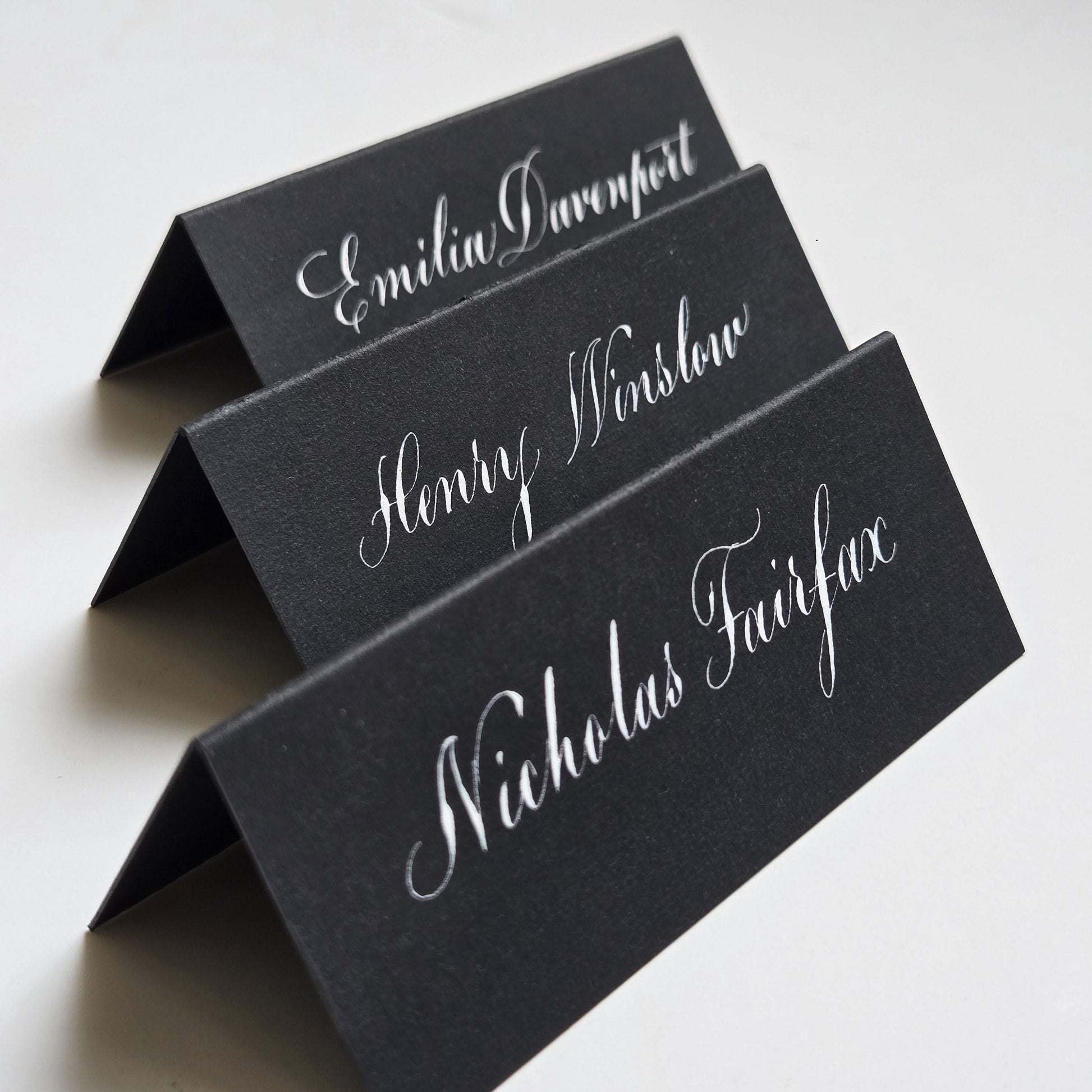 three black name cards with elegant white cursive text printed on them.