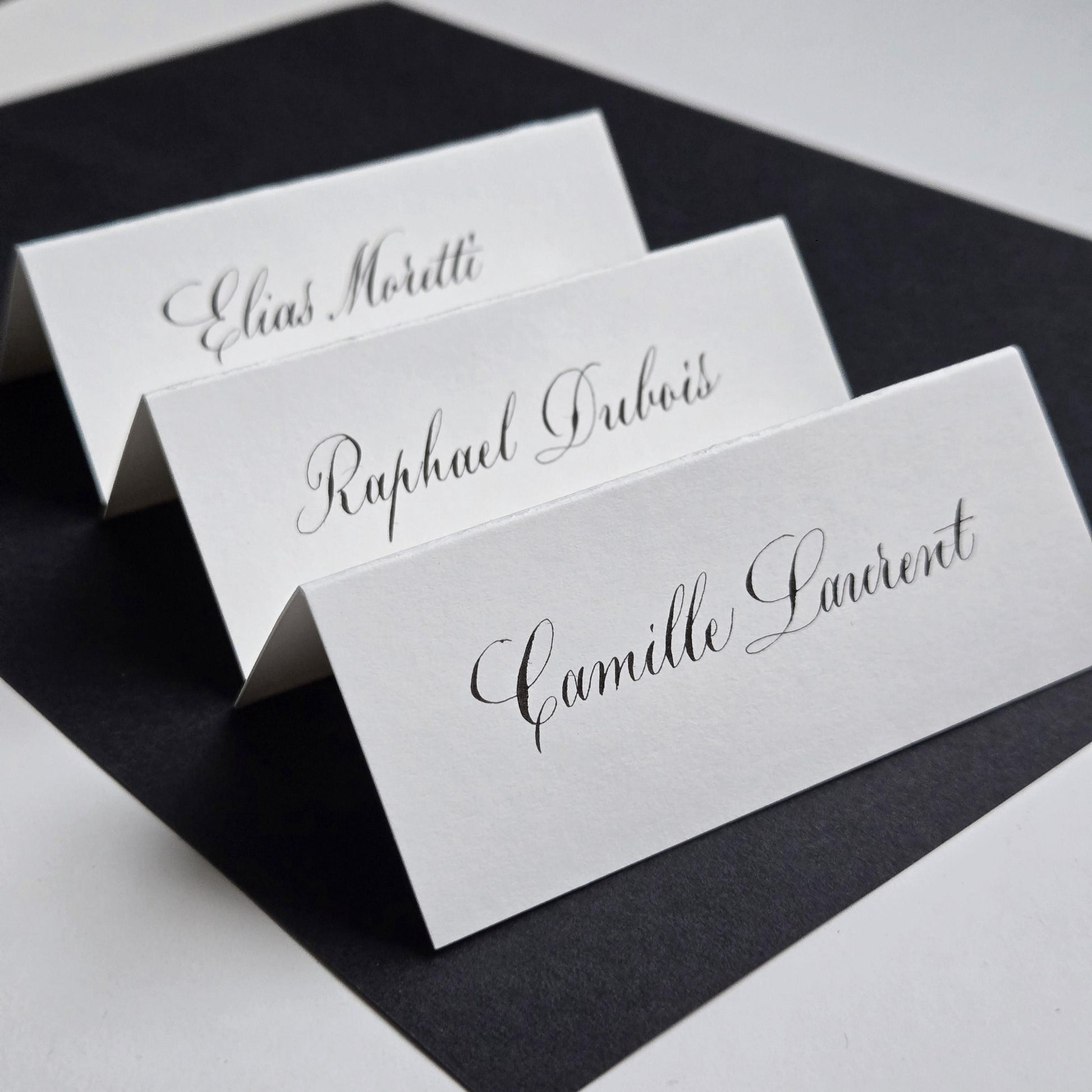 three white name cards with black cursive text, arranged in a row on a black surface.