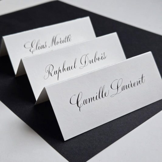 three white name cards with black cursive text, arranged in a row on a black surface.