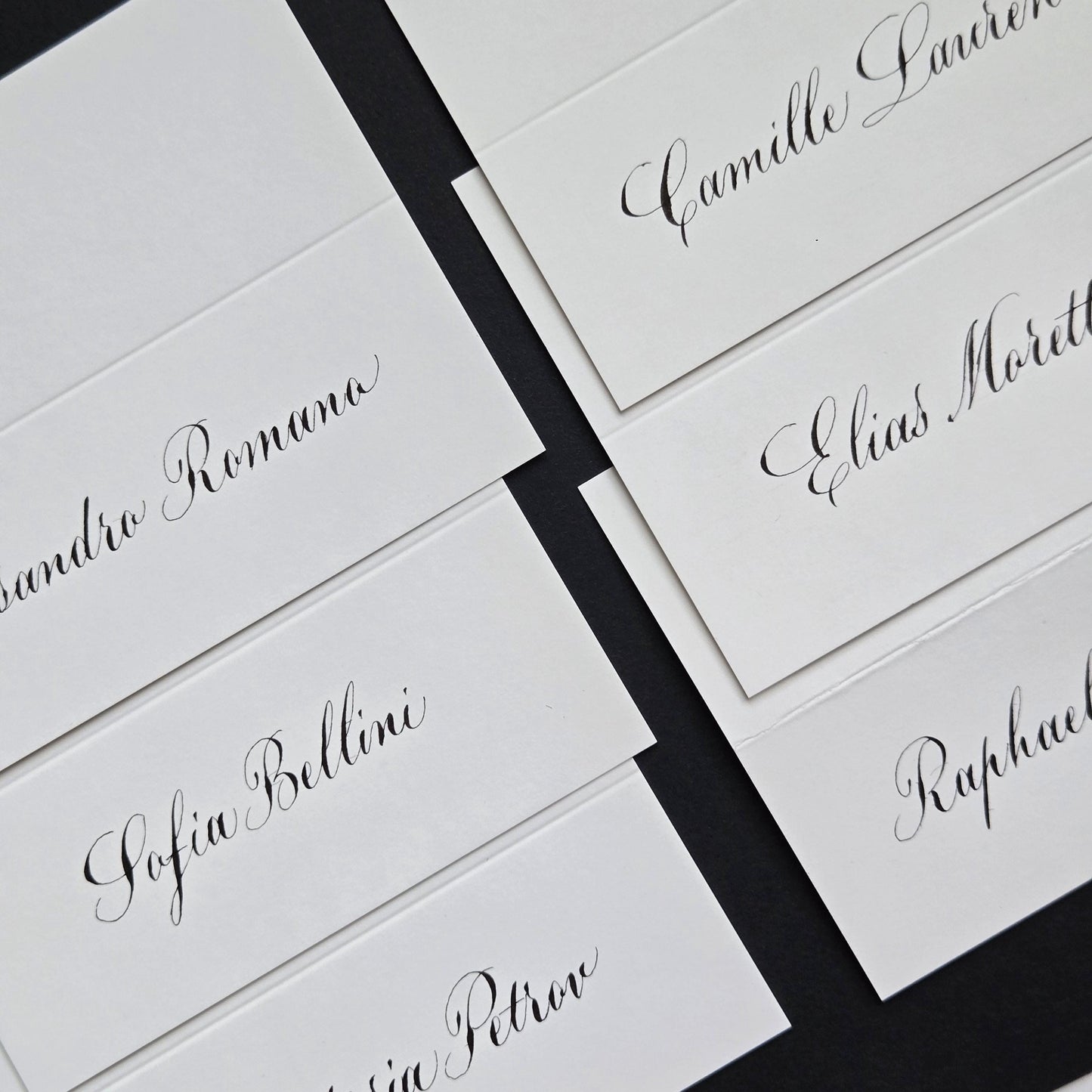 several white name cards with black cursive text, likely for a formal event or gathering.