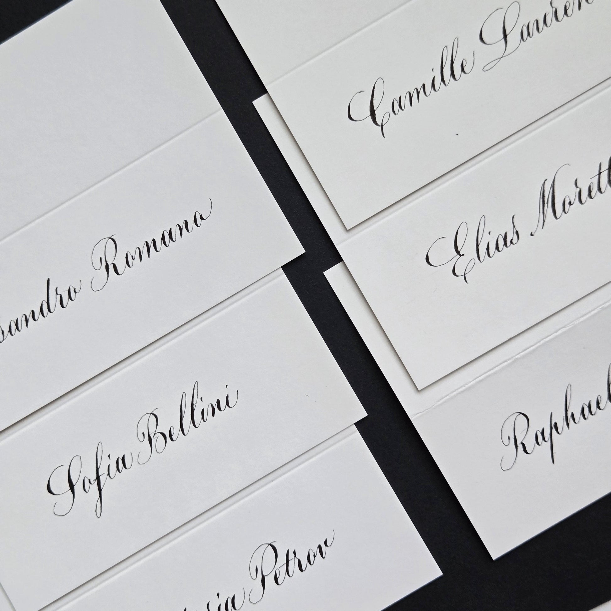 several white name cards with black cursive text, likely for a formal event or gathering.