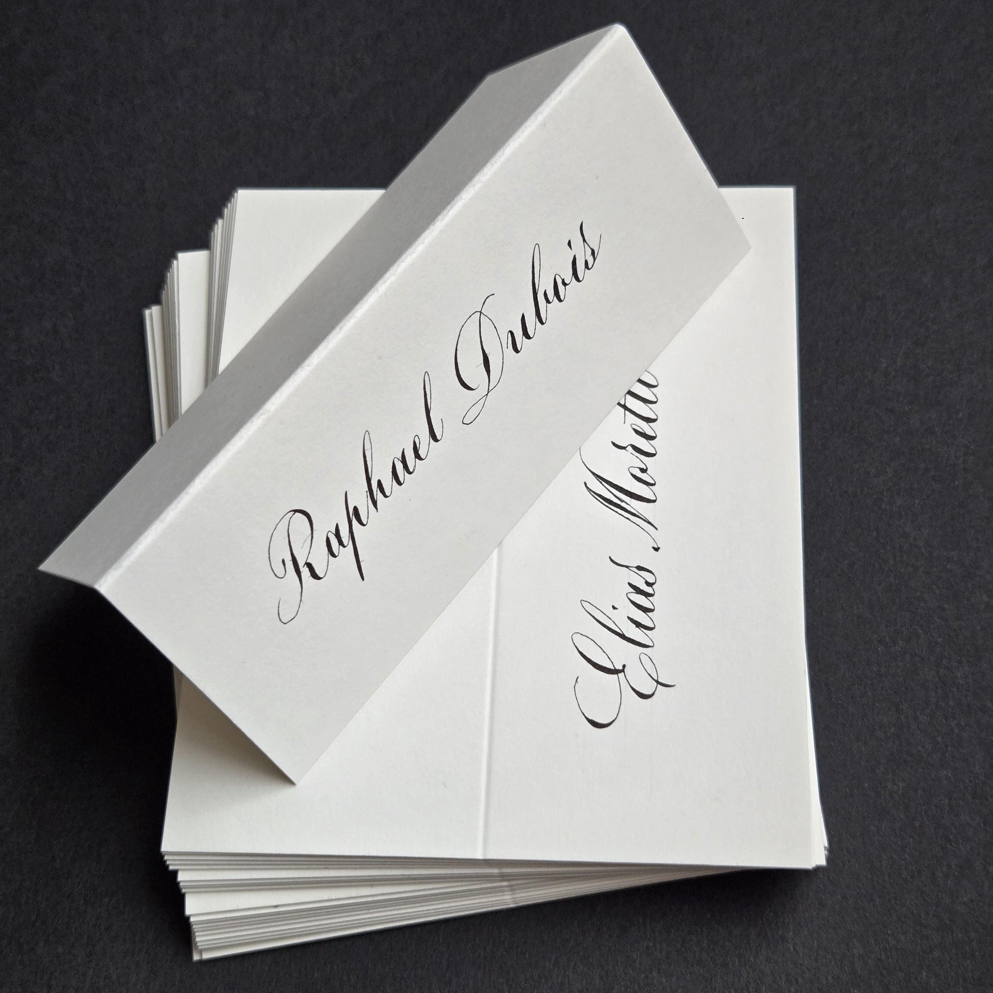 A stack of white paper name cards with elegant cursive text.