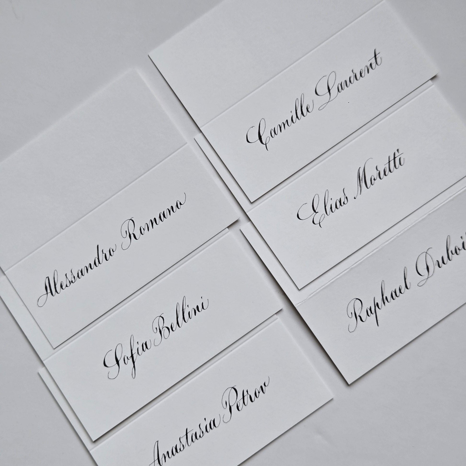 several white name cards with black cursive text, likely for a formal event or gathering.