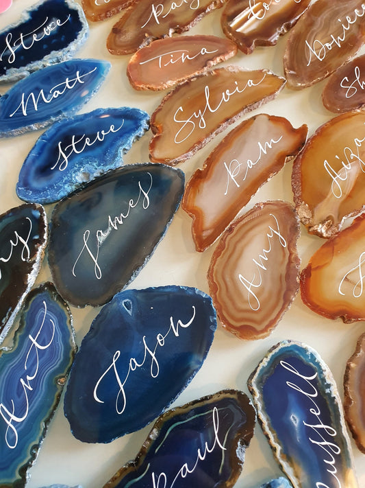 May include: A collection of agate slices with names written in white calligraphy. The agate slices are in shades of blue, brown, and white.