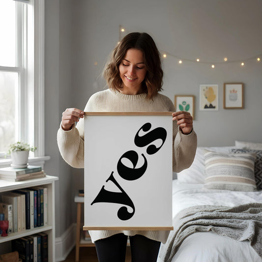 a white desk with a framed poster of the word "Yes" on it, along with a notebook, a cup, and some decorative elements such as a vase and a potted plant.