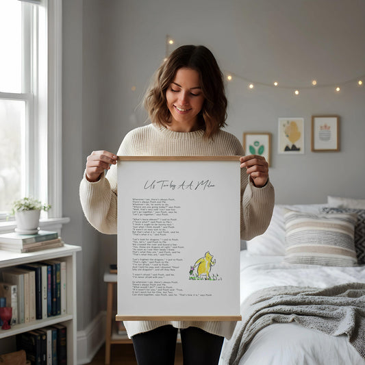 a framed poem titled "Us Today by a Pooh" leaning against a white wall, with a wooden chair and a stack of books placed next to it.