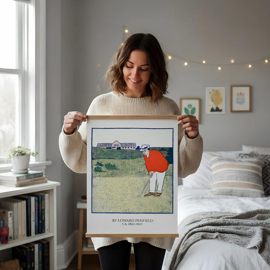 a framed illustration of a golfer on a golf course, with a vase of dried flowers and a cup of coffee on a desk in the foreground.