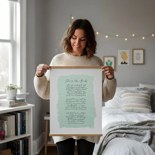 a framed print of a poem on a white desk, accompanied by a notebook, a cup, and a vase with dried flowers.