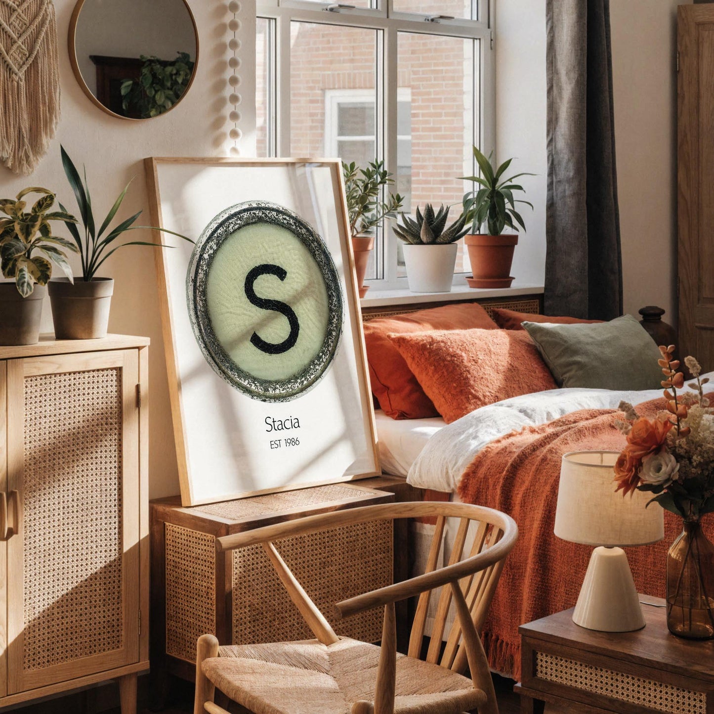 a framed poster with a large letter 'S' on it, placed on a white desk. The desk also has a notebook, a cup, and a vase with dried flowers.