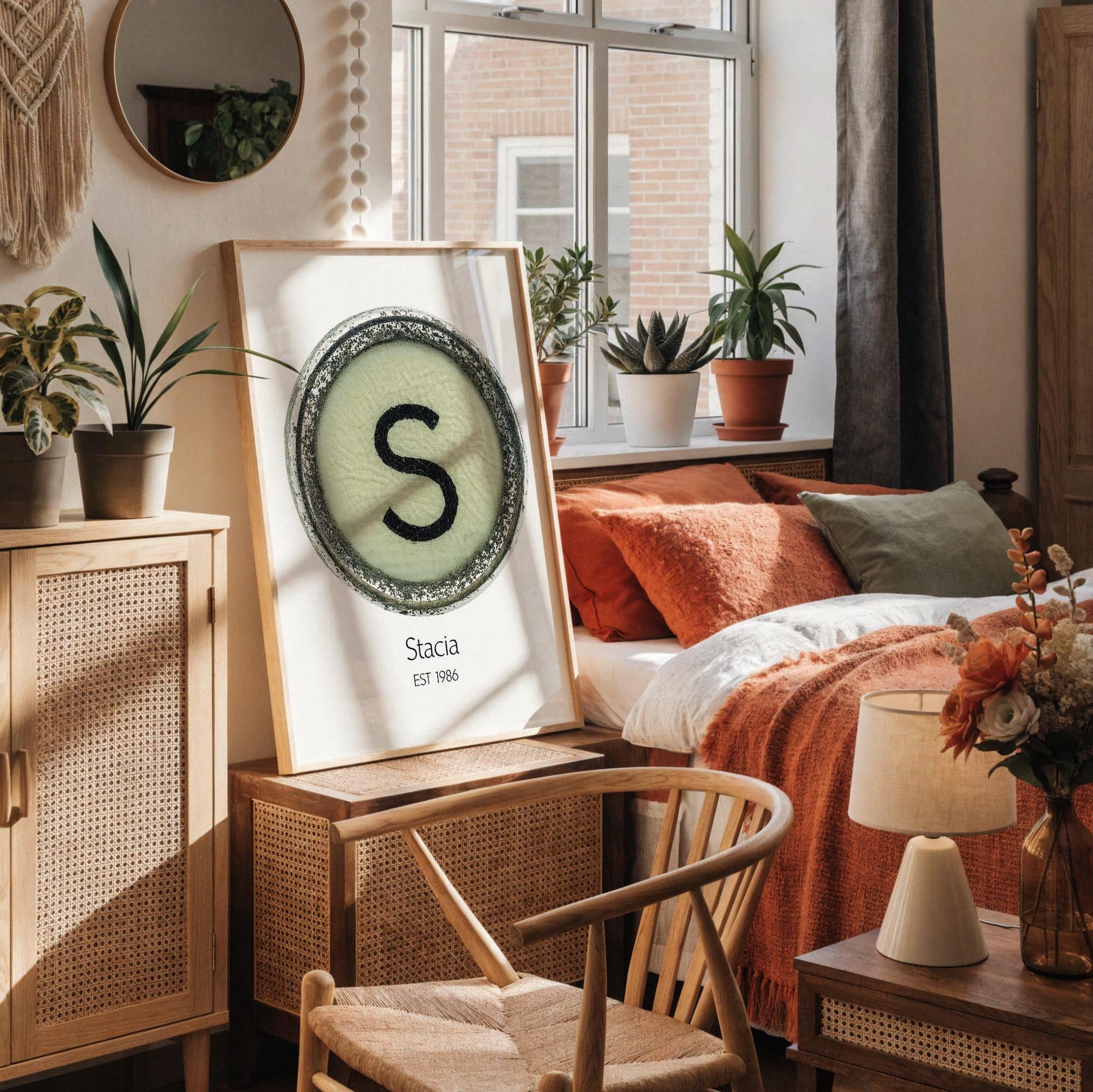 a framed poster with a large letter 'S' on it, placed on a white desk. The desk also has a notebook, a cup, and a vase with dried flowers.