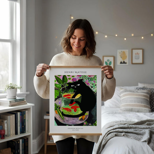 a framed painting of a black cat sitting in a fish bowl, surrounded by colorful fish and plants, placed on a white desk.