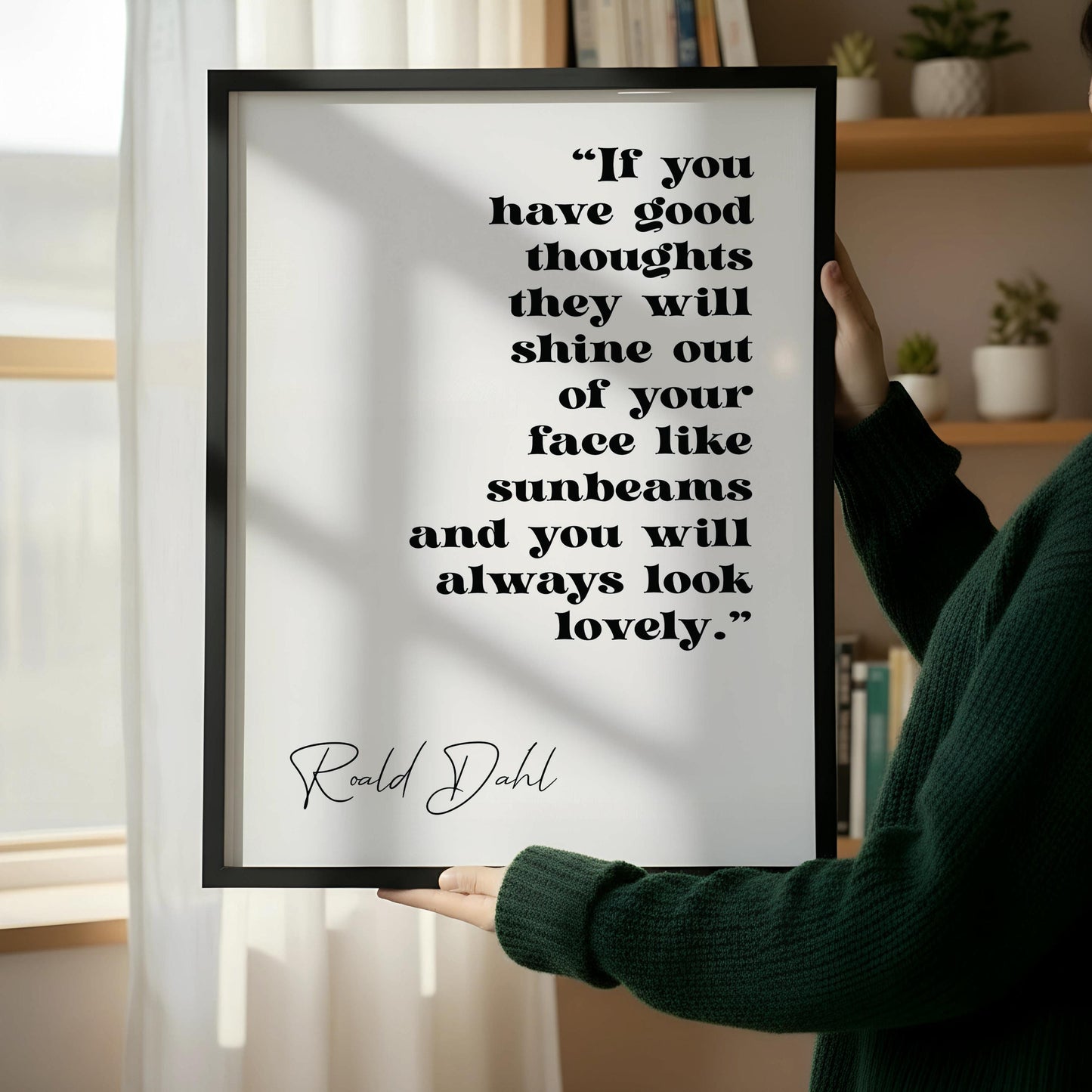 a framed quote by Ralph Dahl, "If you have good thoughts they will shine out of your face like sunbeams and you will always look lovely." The quote is displayed on a white wall, with a wooden chair positioned next to it.