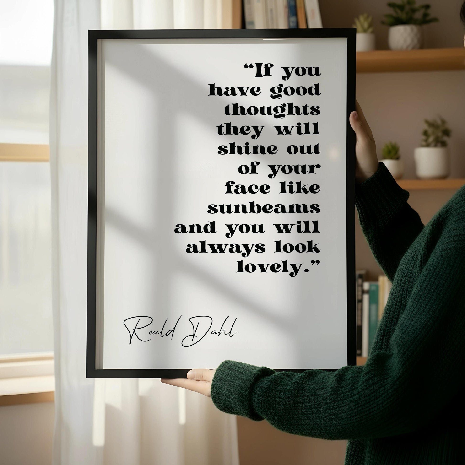 a framed quote by Ralph Dahl, "If you have good thoughts they will shine out of your face like sunbeams and you will always look lovely." The quote is displayed on a white wall, with a wooden chair positioned next to it.