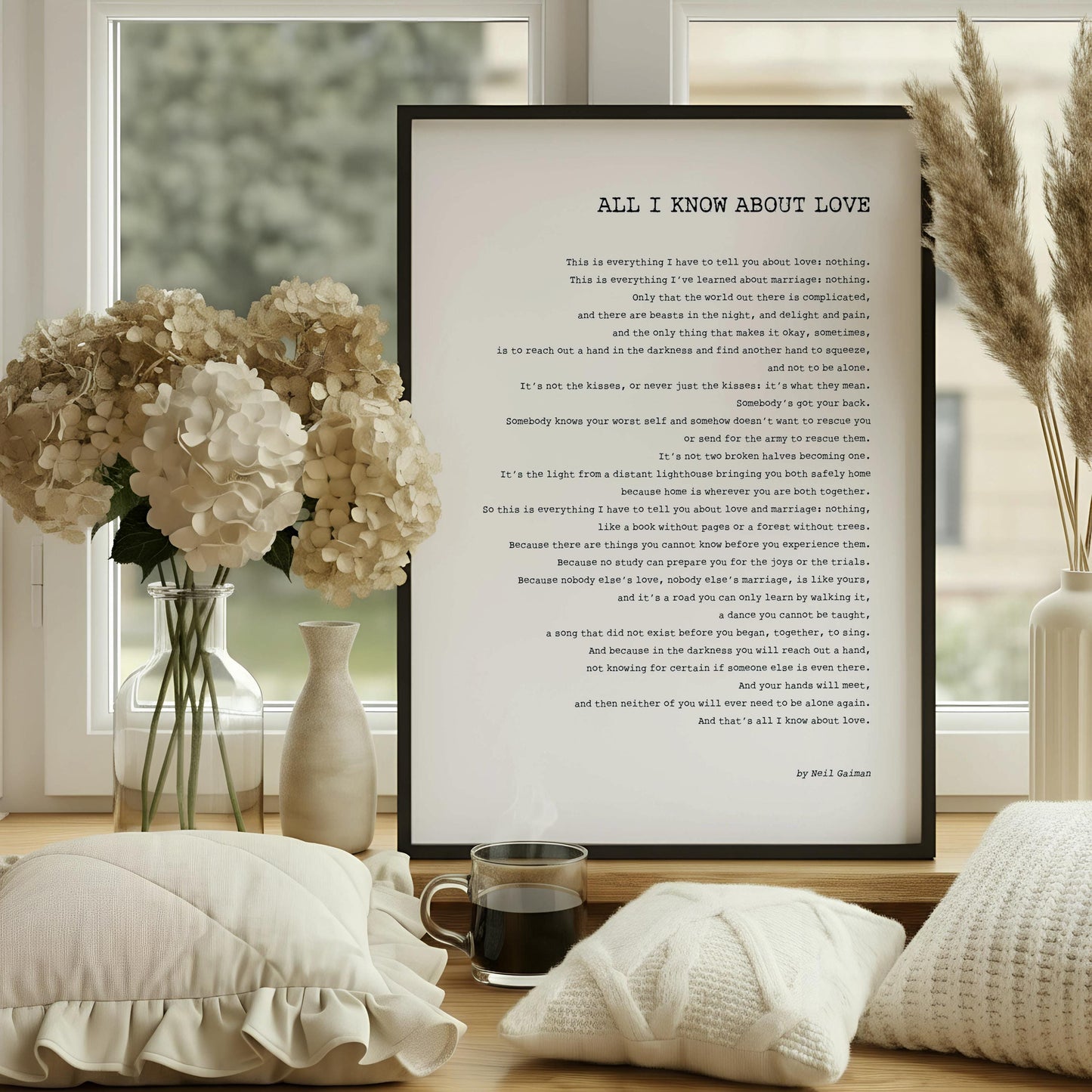 a framed poem titled "All I Know About Love" displayed on a white desk, with a notebook, a cup, and a vase of dried flowers nearby.